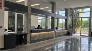 Recepción moderna con mostrador de atención, grandes ventanales, columnas de hormigón y suelo pulido.