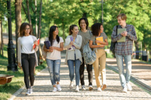 Grupo de estudiantes caminando por un parque con libros y carpetas en la mano.
