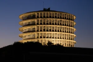Edificio circular iluminado de noche con varias plantas y fachada de hormigón.